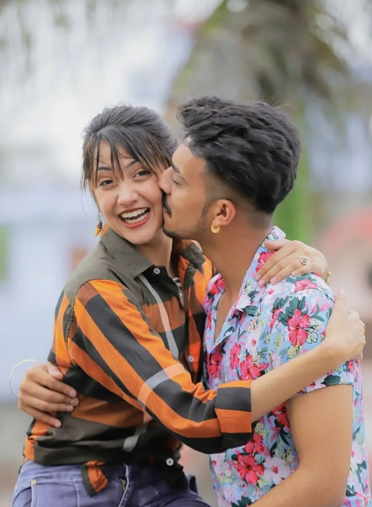 Candid Cheerful Outdoor Portrait of Young Couple with Cheek Kiss