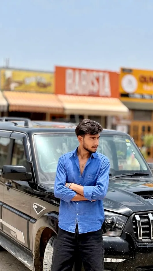 Candid Medium Outdoor Portrait of Young Indian Man Leaning on Black SUV